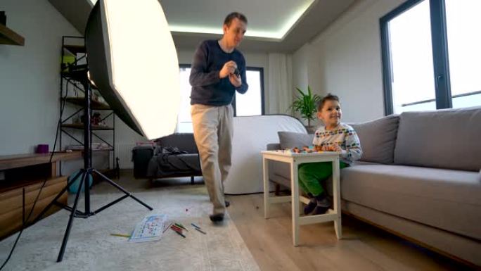 年轻的父亲在家中用相机拍摄儿子的照片，以进行股票摄影