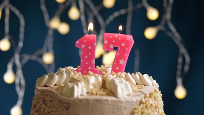 蓝色背景上有17个粉色蜡烛的生日蛋糕。蜡烛吹灭了。慢动作和特写视图