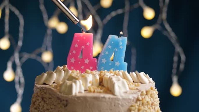 蓝色背景上有44号粉色蜡烛的生日蛋糕。蜡烛着火了。慢动作和特写视图