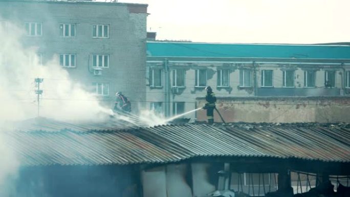 梯子上的消防员或消防员在公寓房屋顶上用烟雾扑灭燃烧的火焰