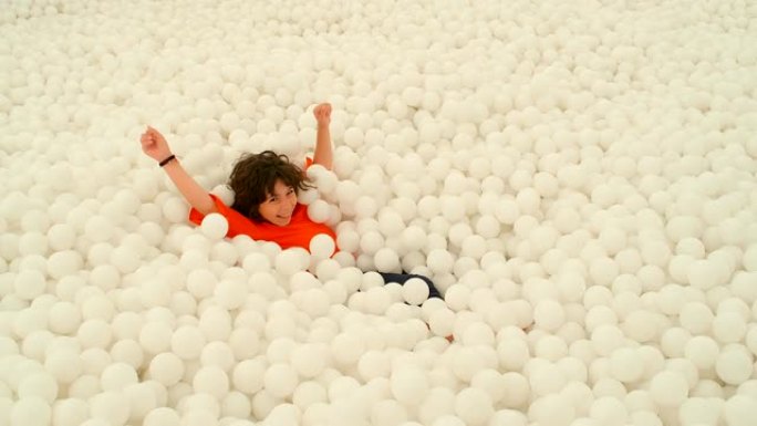 一个可爱的9-10岁女孩在一个球坑里的许多白球中玩耍。4k慢动作