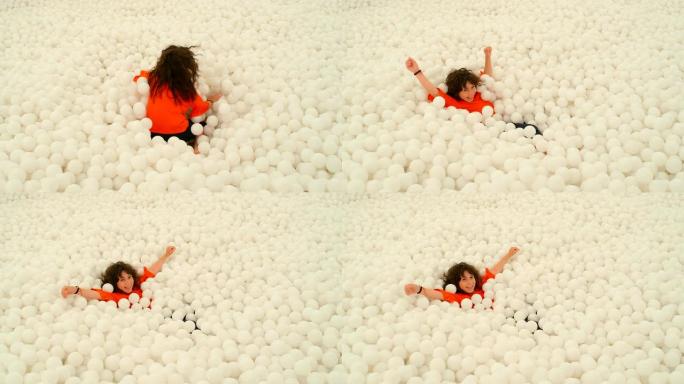 一个可爱的9-10岁女孩在一个球坑里的许多白球中玩耍。4k慢动作