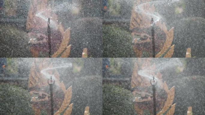 洒水器在花园里喷水，背景是龙雕像。焦点从洒水器转移到雕像