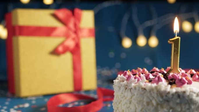 白色生日蛋糕1号点火器燃烧的金色蜡烛，蓝色背景带灯和用红丝带绑起来的礼物黄色盒子。特写