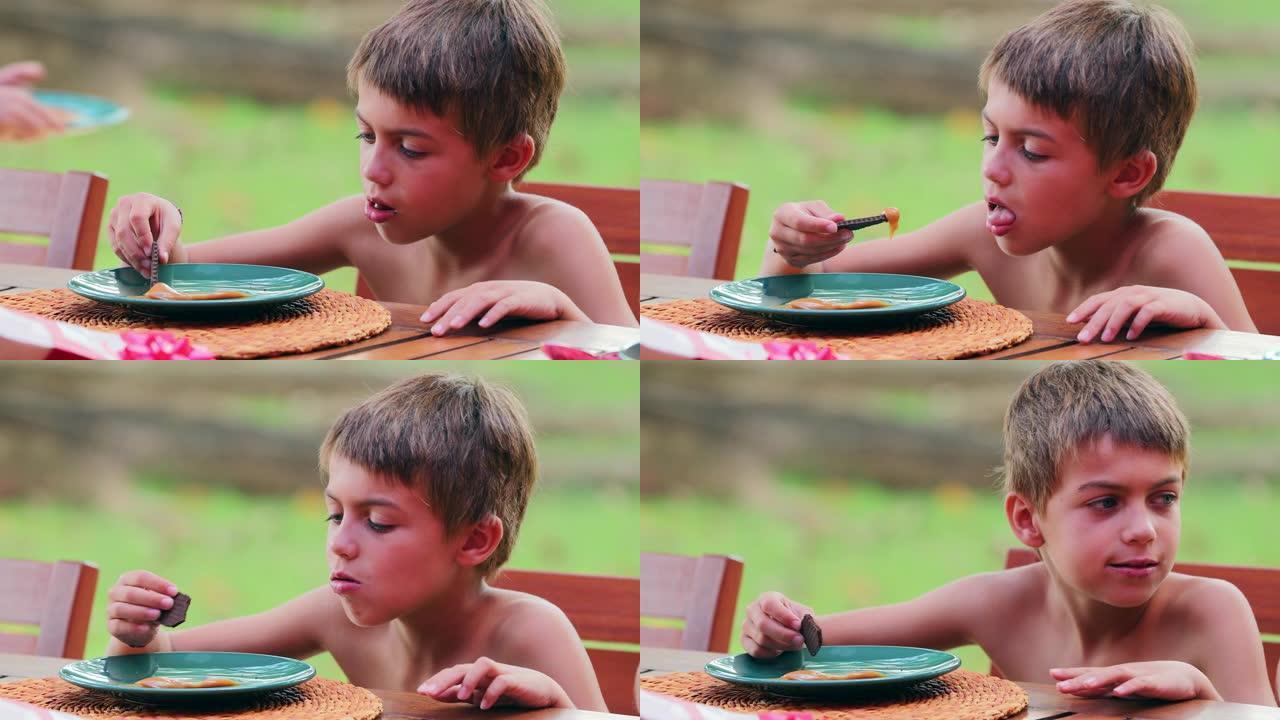 孩子在外面的桌子上吃炊具，小男孩用dulce de leche sweet覆盖饼干