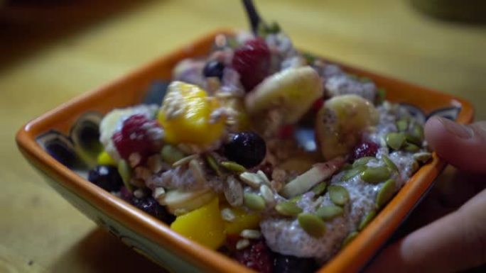 用手将健康的早餐碗与水果，坚果和chia混合在一起
