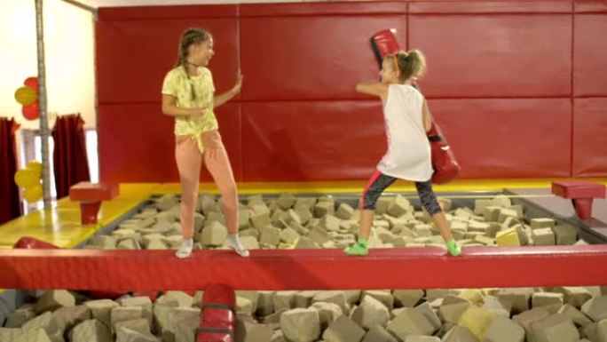 两个中学年龄的女孩用柔软的滚轮愉快地互相推动。角斗士。蹦床公园的乐趣