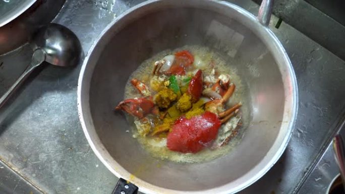 厨师在厨房里用咖喱粉烹饪炸蟹，亚洲流行的海鲜菜单。桌上放着咖喱粉，洋葱，甜椒和鸡蛋炒螃蟹。