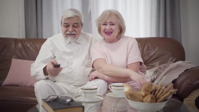 正面成熟的白人夫妇在晚上看电视的肖像。快乐的高级夫妻在室内一起休息。休闲，快乐，生活方式，永恒的爱情