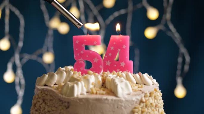 蓝色背景上有54号粉色蜡烛的生日蛋糕。蜡烛着火了。慢动作和特写视图