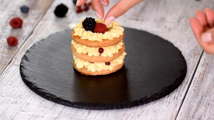 糕点厨师用奶油冻和浆果制作法国Mille Feuille。法式甜点千层酥和奶油。