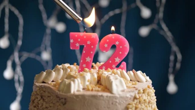 蓝色背景上有72号粉色蜡烛的生日蛋糕。蜡烛着火了。慢动作和特写视图