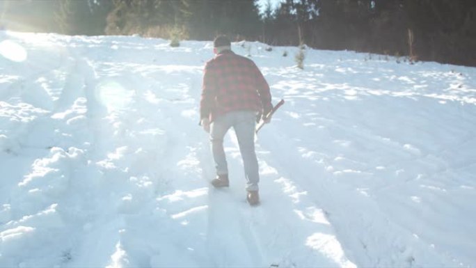 残酷的伐木工人带着斧头沿着雪坡走