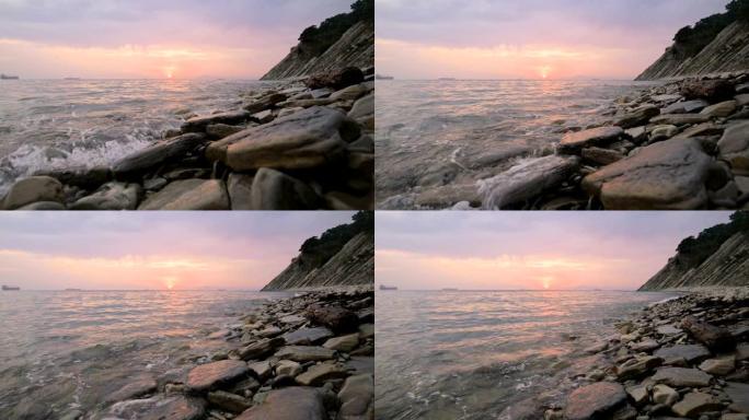 特写慢动作低广角小海浪在岩石海滩上滚动。沿着海滩向前移动。海边。鹅卵石岩石海滩上的日落