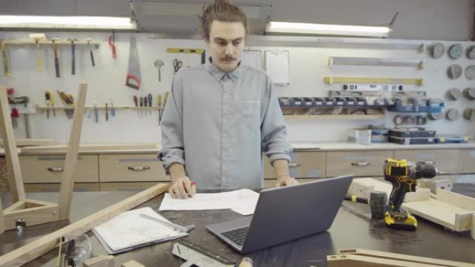 高加索木匠在车间处理笔记本电脑和技术图纸