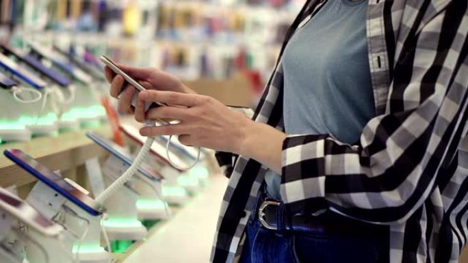 无法辨认的女人的手的腰部照片在一家电子商店选择了智能手机。她从柜台拿走智能手机并尝试使用它。侧视图