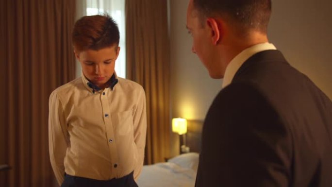 男孩在旅馆房间里系领带，父亲在西装上与儿子说话