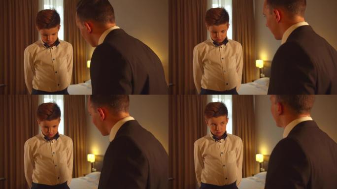 男孩在旅馆房间里系领带，父亲在西装上与儿子说话