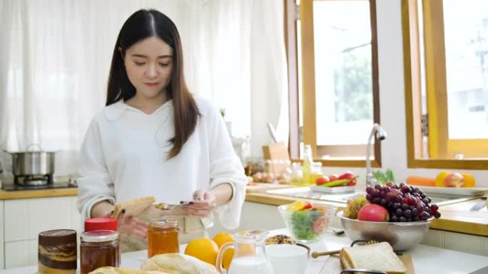 快乐的亚洲女人在厨房的面包上撒上果酱，健康的饮食和健康的理念。