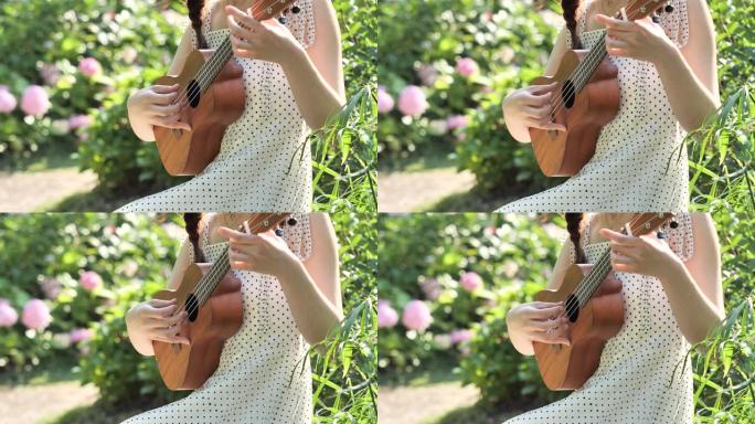 一个穿着衣服的女人的手的特写镜头，在花园里拿着乌克丽莱琴，背景模糊公园，4k镜头，慢动作。