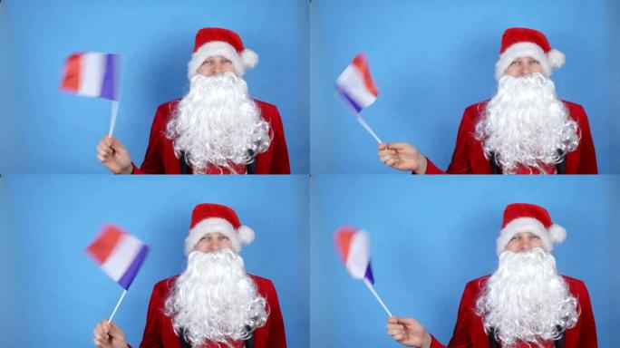 一个穿着圣诞老人服装的男人，留着胡须，在蓝色背景上挥舞着法国国旗。世界新年假期概念