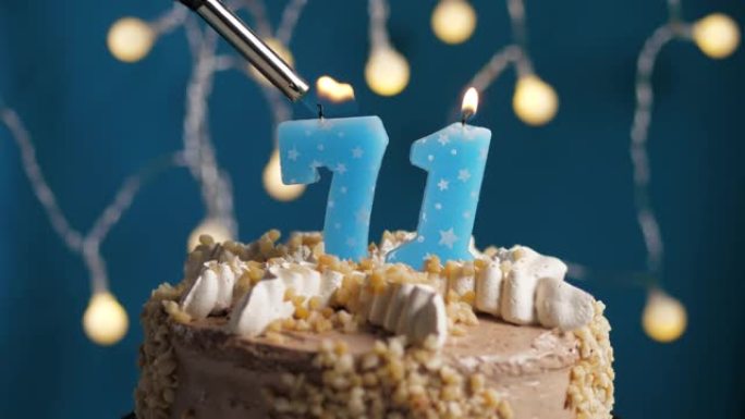 蓝色背景上有71号蜡烛的生日蛋糕。蜡烛着火了。慢动作和特写视图