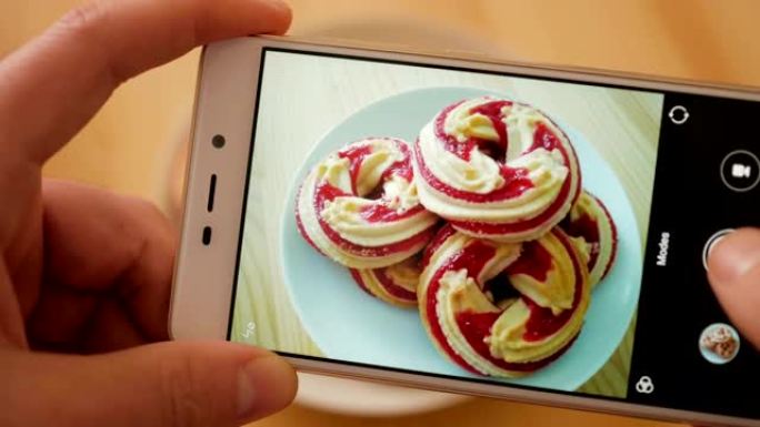 手机上手工制作甜蜜甜点照片的特写。男性在智能手机上的照片木制桌子上的圆形软饼干关闭。