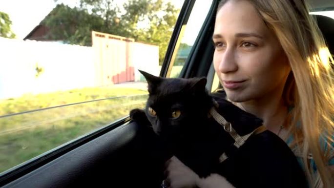 一个年轻女孩在驾驶汽车的后座上抱着一只黑猫，他们一起看着窗外。特写。从车内看。4K