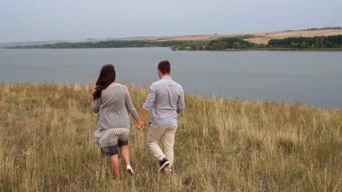 日落时牵手走在田野里的年轻夫妇。