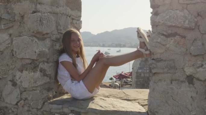酷酷快乐的女孩坐在古老的石墙上