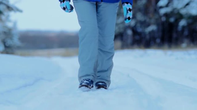 踏着雪地，一个女人在雪道上踩着冬鞋。冬天在树林里的雪地里散步。特写。