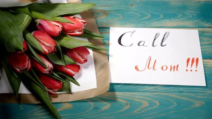 木桌上的Call Mom消息便笺和郁金香花束的俯视图。爱情关系概念。母亲节。4 k拍摄