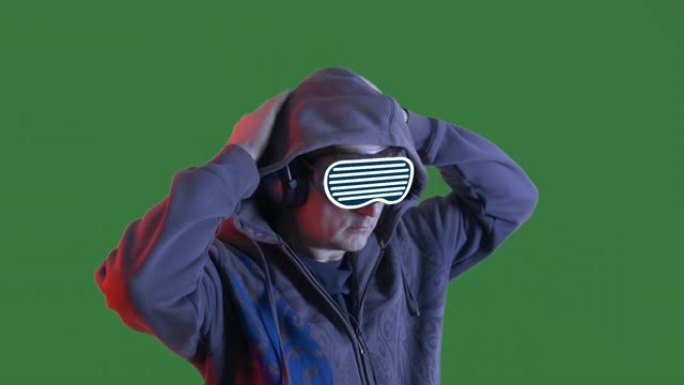 秃头男人听音乐在耳机和VR眼镜在绿色的chromakey背景。戴着黑色兜帽和虚拟现实眼镜的人在耳机里