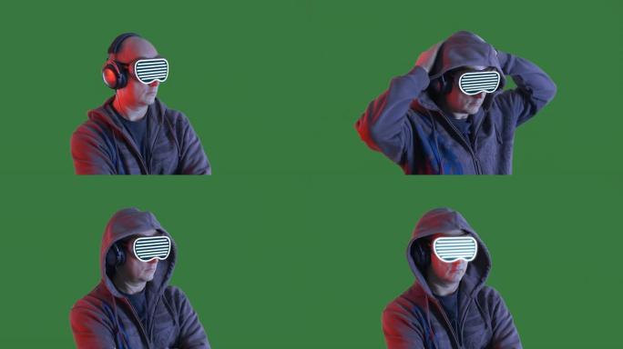 秃头男人听音乐在耳机和VR眼镜在绿色的chromakey背景。戴着黑色兜帽和虚拟现实眼镜的人在耳机里