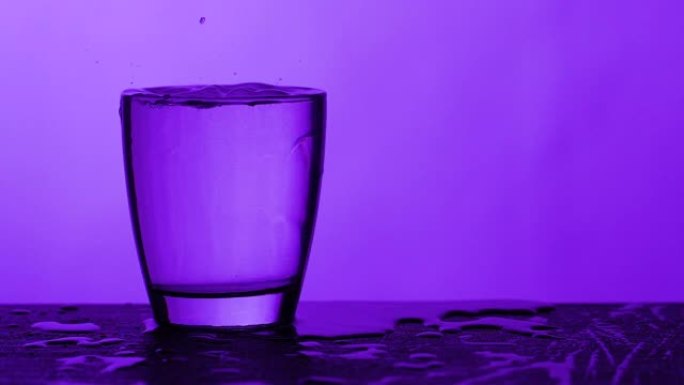 雨滴落在装满水的玻璃上-紫色背景