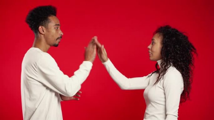 年轻的非洲夫妇在红色工作室背景下用手势做有趣的问候，就像老电影一样。穿着白色衣服的漫画男人和女人。