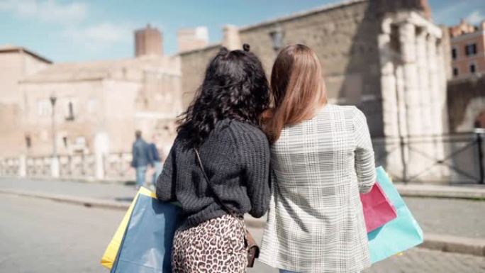 迷人的时尚女孩与彩色纸购物袋在市中心自拍照片。两名模特在街上喝aperetif鸡尾酒，配杯橙色饮料，