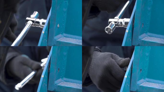 戴上防护手套的男人用扳手松开螺栓，将螺栓放在金属蓝色结构上。夹。拆卸金属结构