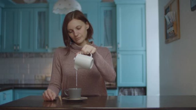 30多岁的年轻女性将牛奶从锅里倒入一杯咖啡中。女人喝杯咖啡闻起来。咖啡享受过程。