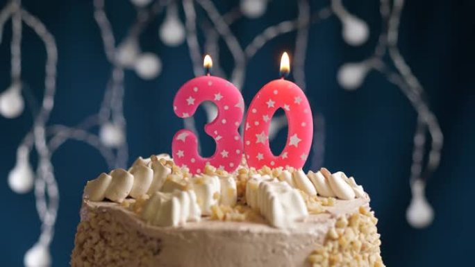 蓝色背景上有30号粉色蜡烛的生日蛋糕。蜡烛吹灭了。慢动作和特写视图