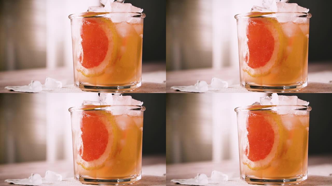 酒保将冰块放入玻璃中，慢动作。葡萄柚鸡尾酒，特写。