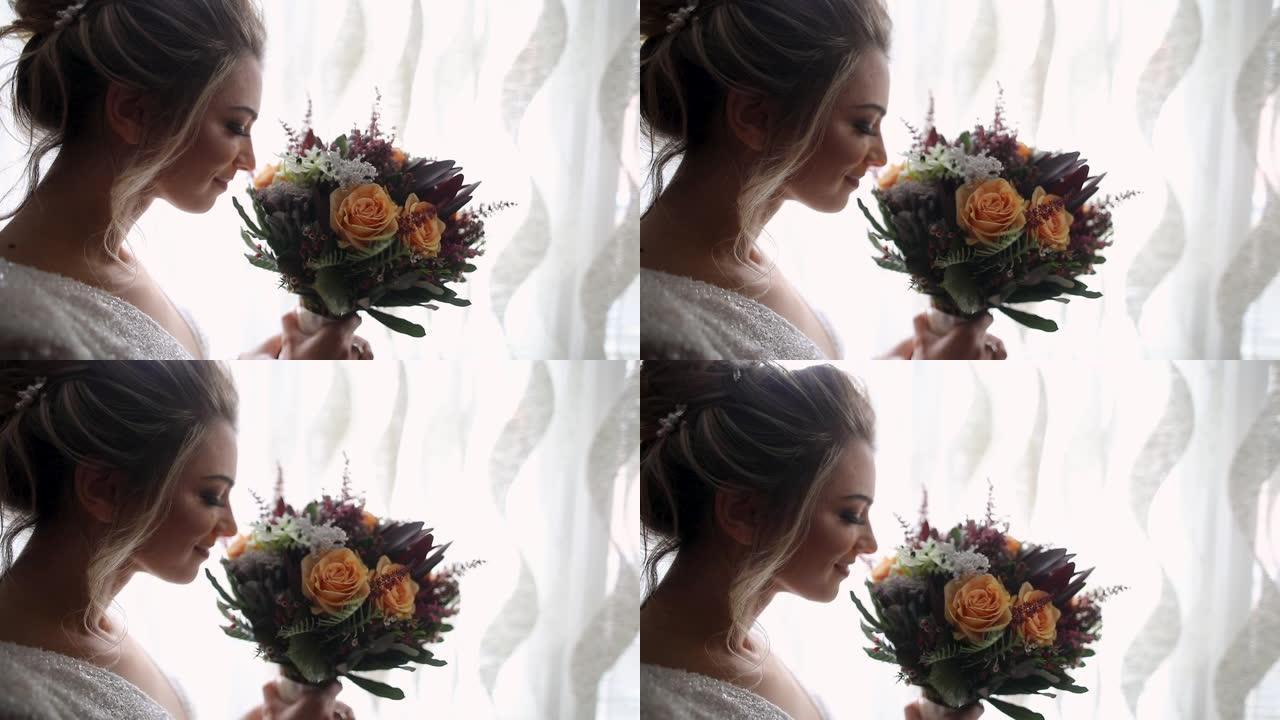 美丽的年轻女子站在窗户附近，拿着并闻到华丽的婚礼花束