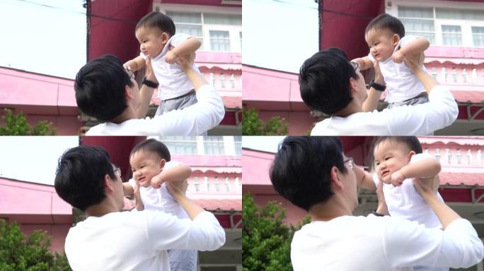 慈爱的父亲举起快乐的亚洲婴儿，站在他们家门前与孩子玩耍