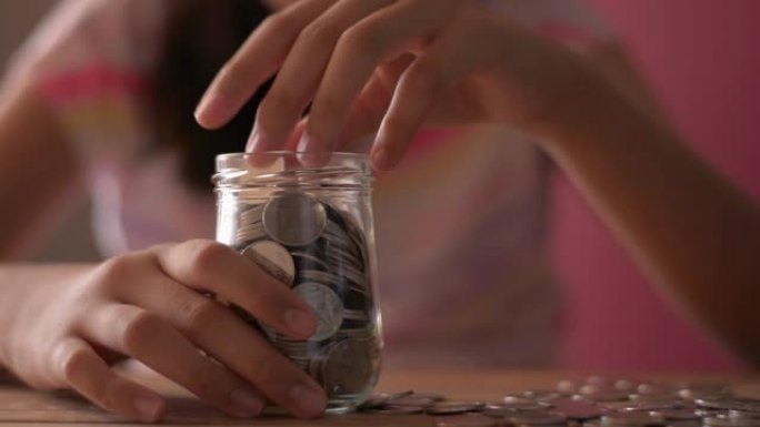 穿着便装的小女孩把钱放进玻璃罐里，以备将来之用。