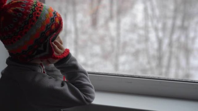 一个小男孩透过窗户看着大雪，等待圣诞节的到来