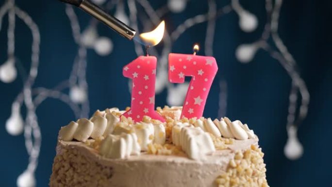 蓝色背景上有17个粉色蜡烛的生日蛋糕。蜡烛着火了。慢动作和特写视图