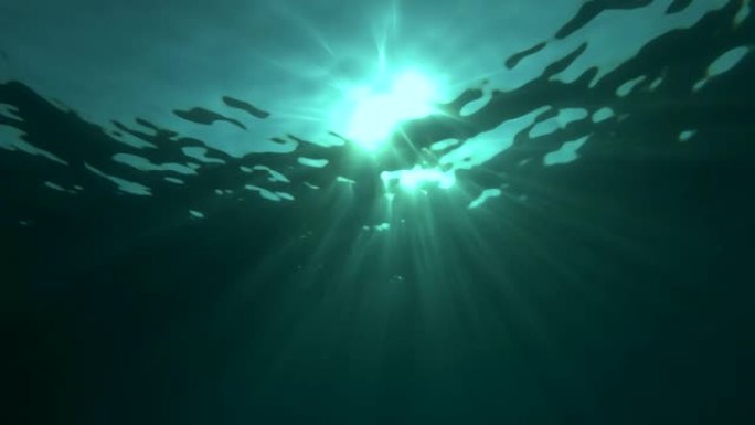 慢动作，阳光穿透水面。水下光线创造了一个美丽的面纱，由阳光组成。水下海浪随着光线振荡和流动
