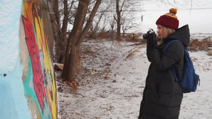 一个女孩在冬天在墙上拍摄涂鸦。女游客在街上拍照。