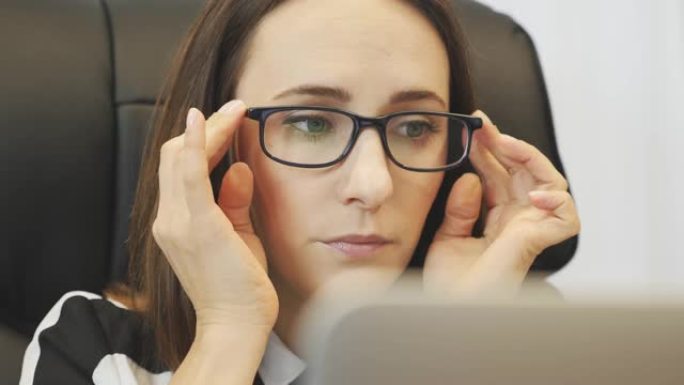 专注的女人在笔记本电脑工作前戴上眼镜。在笔记本电脑屏幕上看女性脸的特写。自信的女商人在办公桌前用笔记