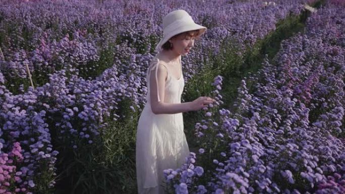 一个年轻的女人在阳光明媚的日子里轻轻地手里拿着鲜花，闻到紫色的花朵。慢动作